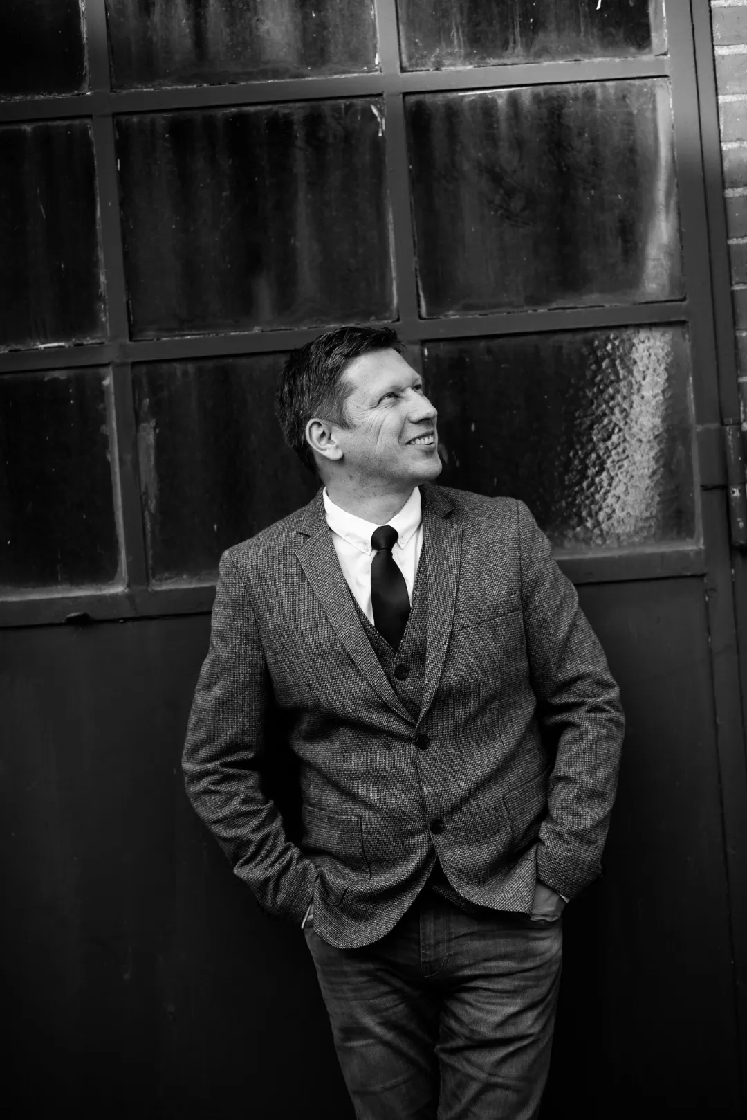 Black and white portrait of Sven Rahmsdorf against a warehouse window